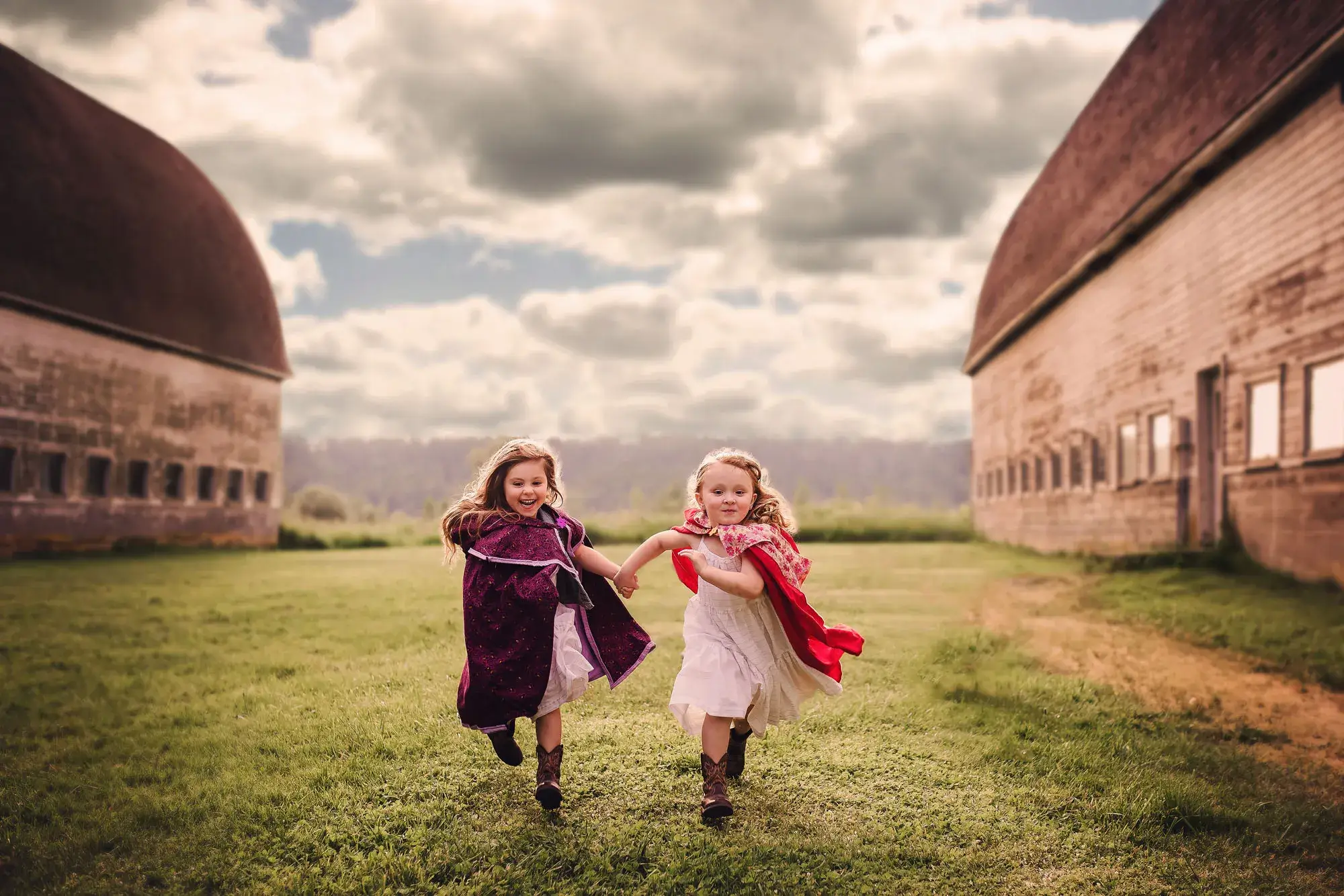 Two children running hand in hand between barns